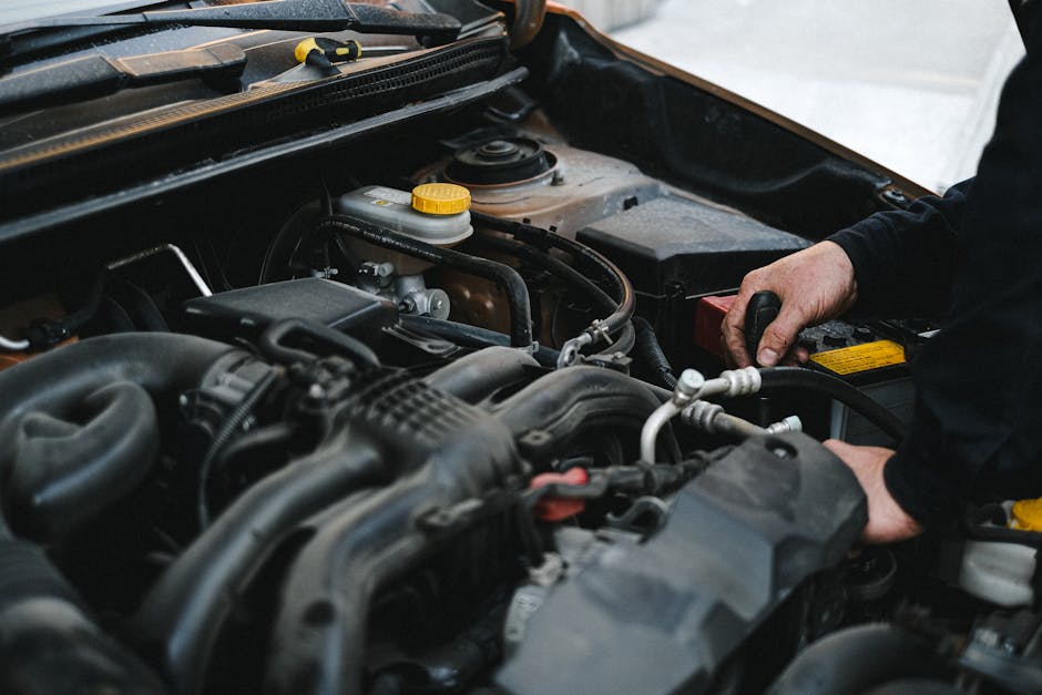 Mâini de mecanic lucrând în compartimentul motor, lângă bateria mașinii
